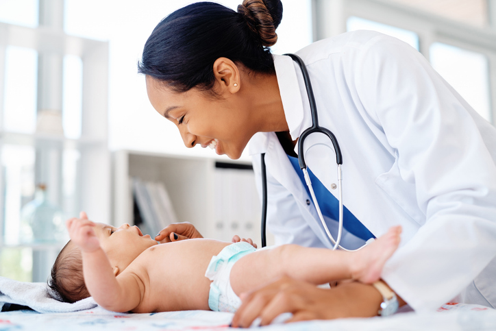 Physician smiling to an infant as they are laying on exam table