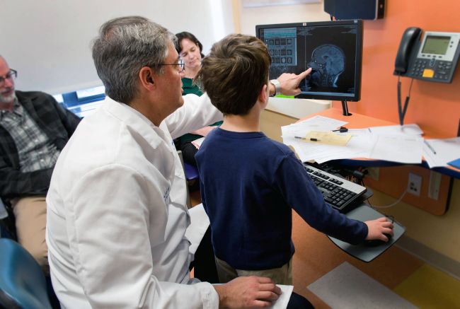 Mustafa Sahin shows a neurology scan to child on a computer monitor