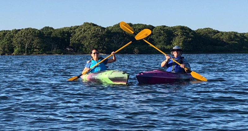 Kenan Haver and his wife in two kayaks raising their paddles