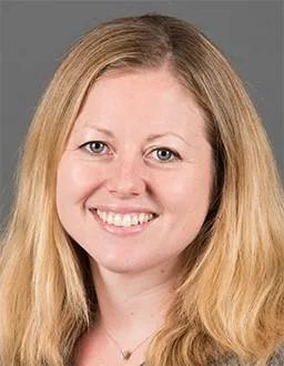 Headshot of Olha Halyabar, a woman with blonde hair in front of a grey background.